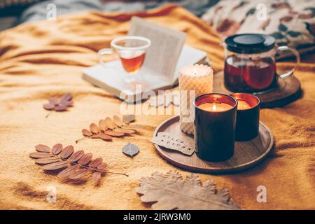 Automne confortable à la maison. Bougies allumées avec carte hello automne, tisane dans verre tasse et livre ouvert sur le écossais jaune. Lecture, détente, loisirs à Banque D'Images