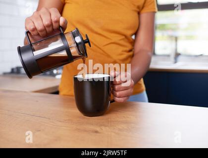 Un gros plan d'une jeune femme qui verse du café de la presse française dans une tasse dans la cuisine Banque D'Images