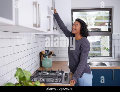 Une jeune femme multi-ethnique entre dans ses placards de cuisine Banque D'Images