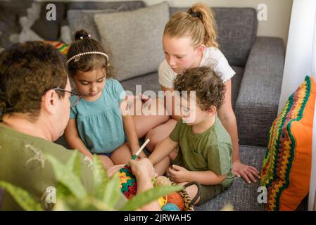 Femme de haut rang passant une journée avec ses petits-enfants, triant la place de la granny à la maison. Deux filles, grand-mère et un drôle de jeune garçon en crochet, c'est un passe-temps à l'ancienne qu'ils aiment faire. Banque D'Images