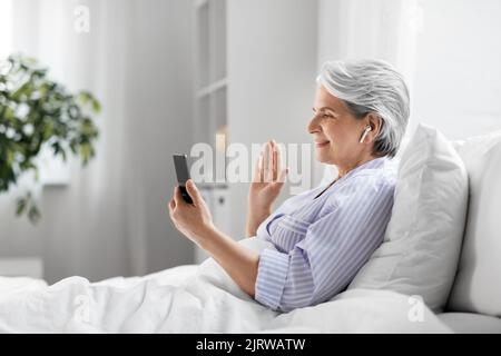 femme âgée avec téléphone et appel vidéo au lit Banque D'Images