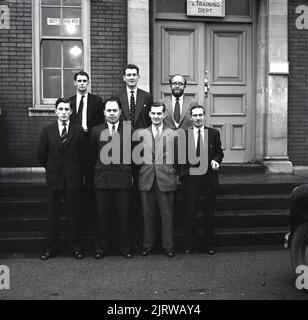 1950s, historique, cadres de la Steel Company of Wales (SCOW) debout pour une photo de groupe à l'extérieur des bureaux, Port Talbot, pays de Galles, Royaume-Uni. Le panneau indiquant la porte indique Avis du service de la formation dans la fenêtre, dit : semaine des chaussures de sécurité. En 1950s, le gouvernement a adopté une nouvelle loi réglementant la production de chaussures de sécurité. Cela signifie que les bottes en cuir à semelle ne pouvaient plus être portées dans les environnements industriels et que de nouveaux matériaux devaient être utilisés pour répondre aux exigences de la nouvelle réglementation. Banque D'Images