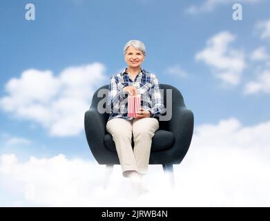 femme âgée mangeant du pop-corn assis dans un fauteuil Banque D'Images