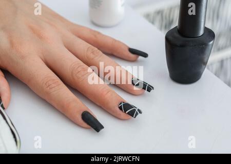 main d'une fille de latina, placée sur la table, avec ses ongles peints en noir avec des bandes blanches à côté d'elle un vernis à ongles noir mat pour la peinture et desi Banque D'Images