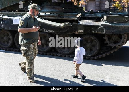 Un garçon et un homme en uniforme militaire se promo devant un char russe brûlé. Une exposition de matériel russe détruit est organisée à Khreshchatyk. Il y a six mois, les troupes militaires russes étaient déployées par le président russe Vladimir Poutine pour envahir l'Ukraine. Il aurait estimé qu'ils auraient capturé Kiev dans trois jours, Banque D'Images