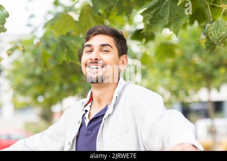 jeune homme qui s'étend les bras devant les arbres dans une ville Banque D'Images