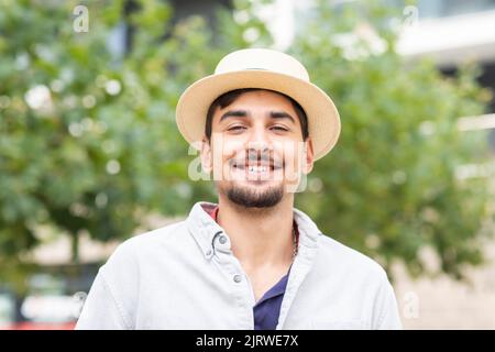 jeune homme avec chapeau d'été debout devant les arbres dans une ville Banque D'Images