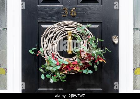 Couronne sur la porte avant avec fleurs rouges et feuilles ou feuillage verts, couronne décorative Banque D'Images