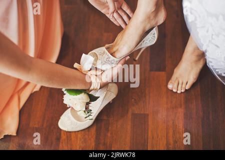 Mariée le matin pendant les préparatifs de mariage. Demoiselle d'honneur aidant avec des chaussures Banque D'Images