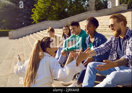 Groupe d'amis joyeux qui parlent, s'amuser et rire assis dans les escaliers de la rue. Banque D'Images