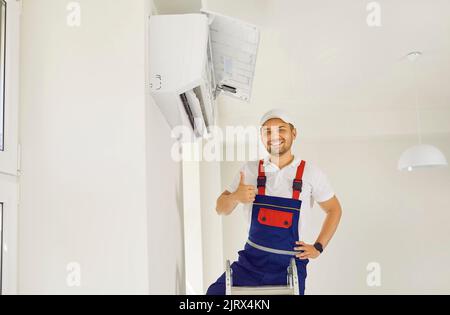 Portrait d'un technicien homme souriant montrant le pouce vers le haut après la mise en service du climatiseur. Banque D'Images