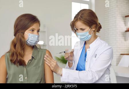 Le médecin du centre de vaccination donne le vaccin Covid 19 à une adolescente qui porte un masque facial. Banque D'Images