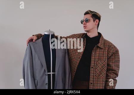 Créateur de mode avec un nouveau vêtement. Couturière travaillant sur un costume gris. Homme de race blanche blonde avec un mannequin sur un fond blanc isolé. Photo de haute qualité Banque D'Images