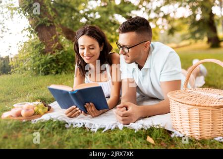 couple heureux lisant le livre sur le pique-nique au parc d'été Banque D'Images