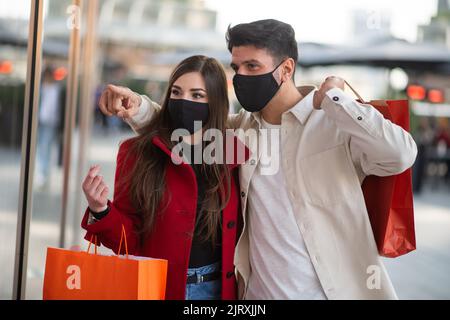 Covid et coronavirus shopping, jeune couple marchant dans une ville tout en portant des sacs de shopping Banque D'Images