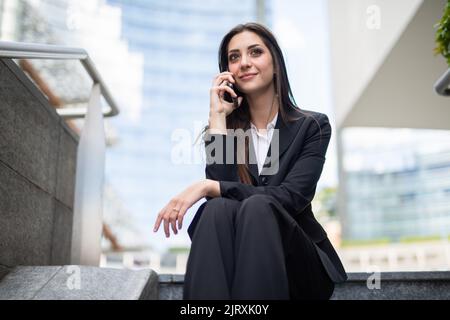 Jeune femme d'affaires parlant au téléphone tout en étant assise sur un escalier Banque D'Images