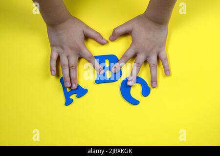 Les mains des enfants tiennent des lettres. Lettres bleues sur fond jaune Banque D'Images
