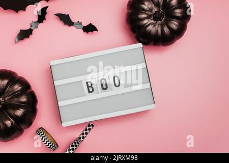 Décor tendance pour Halloween sur fond rose, boîte lumineuse avec texte boo, citrouilles noires et silhouettes de chauve-souris Banque D'Images