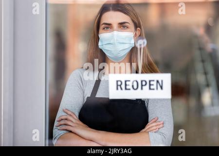 femme dans le masque avec la bannière de réouverture sur la vitre de porte Banque D'Images