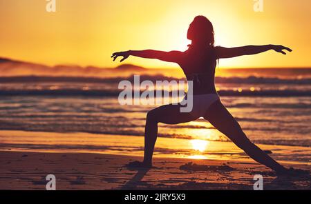 Toutes les bonnes choses sont sauvages et gratuites. Silhouette de jeune femme pratiquant le yoga sur la plage. Banque D'Images
