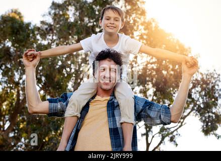 Des ailes en pleine croissance avec l'aide de Dad. Portrait d'un père heureux portant son jeune fils sur ses épaules à l'extérieur. Banque D'Images