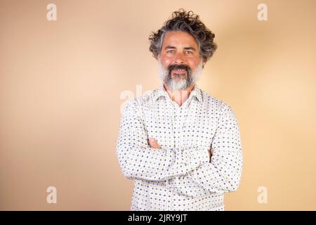 Homme de race blanche d'âge moyen réussi habillé à la légère avec les bras croisés isolé sur fond beige Banque D'Images