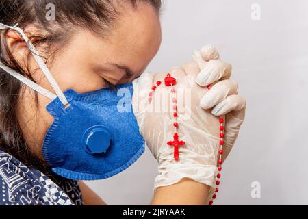 Femme blanche priant portant un masque bleu avec un troisième dans ses mains, protection contre le coronavirus. Au Brésil. Banque D'Images