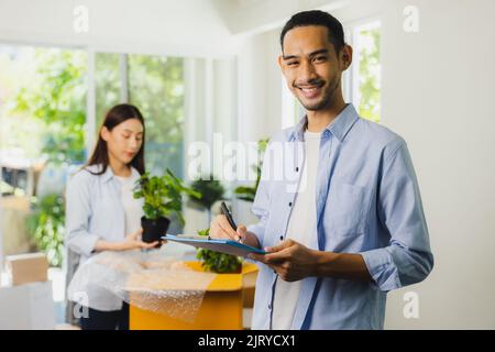Portrait du livreur asiatique, courrier vérifiant la boîte d'emballage avant l'envoi au client Banque D'Images