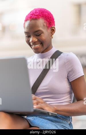 Portrait vertical de la jeune femme afro souriante à l'aide d'un ordinateur portable Banque D'Images