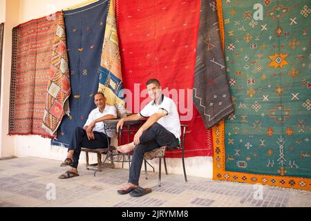 Hommes marocains prenant une pause café, tapis noués à la main accrochés au mur à l'arrière, Meknes, Maroc Banque D'Images