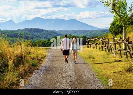 Homme et femme se promenant le long d'une route de terre entre les oliveraies avec les montagnes en arrière-plan et au coucher du soleil. Banque D'Images