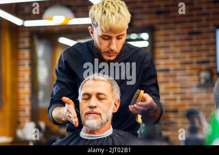 un maître tendance et élégant coupe les cheveux du client de l'homme ancien dans un salon de coiffure moderne Banque D'Images