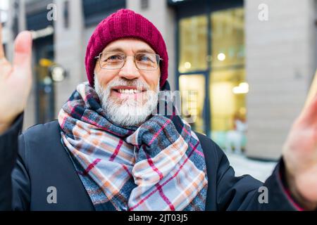 heureux bon regard mature homme faisant un appel vidéo avec sa famille dans le marché d'hiver dans la ville Banque D'Images
