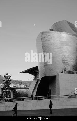 Un cliché vertical du musée Guggenheim de Bilbao en noir et blanc avec la lune en arrière-plan Banque D'Images