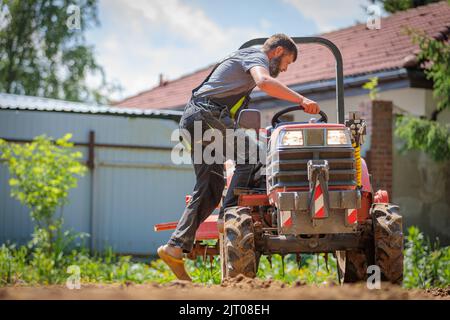 Un homme sur un mini-tracteur nivelle une parcelle de terrain, libère le sol. Banque D'Images