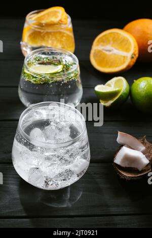 Ensemble de différents cocktails de seltzer sur fond de bois noir. Vue de dessus. Cocktail avec orange citron et noix de coco. Trois boissons froides Banque D'Images