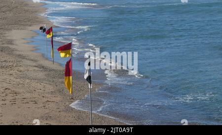 drapeaux de plage rouges et jaunes, y compris drapeaux noirs et blancs le long du rivage à l'extérieur de la plage Banque D'Images