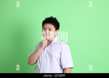 Le garçon asiatique avec l'uniforme étudiant sur fond vert. Banque D'Images