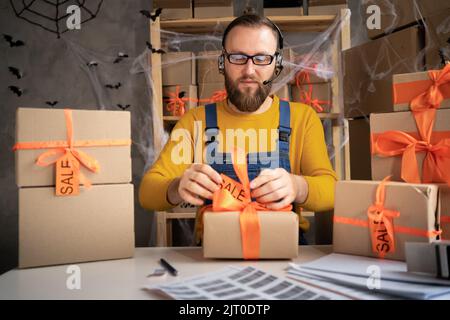 Propriétaire de petite entreprise emballant une boîte pour l'expédition d'Halloween, entrepreneur indépendant travaillant dans le bureau à domicile en utilisant des écouteurs prenant la commande en ligne, SME Banque D'Images