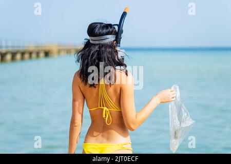 femme en bikini jaune et de la plongée ramasser une poubelle en plastique de la mer Banque D'Images