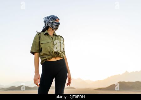 femme avec tête et visage couverts avec foulard à carreaux noir et blanc sur fond désertique Banque D'Images