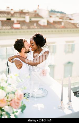Mariée est assis dans les bras de marié à la table sur la terrasse du bâtiment Banque D'Images