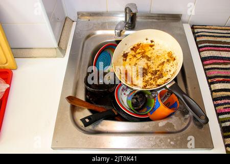 une masse de plats sales avec des restes de nourriture qui attendent d'être lavés dans l'évier métallique après un dîner de fête Banque D'Images