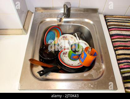 une masse de plats sales avec des restes de nourriture qui attendent d'être lavés dans l'évier métallique après un dîner de fête Banque D'Images