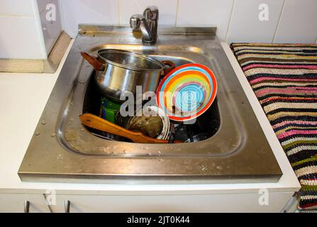 une masse de plats sales avec des restes de nourriture qui attendent d'être lavés dans l'évier métallique après un dîner de fête Banque D'Images