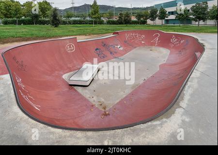 Parc de skate en béton, parc de skate vide, avec des arbres quelques graffitis et ciel nuageux Banque D'Images