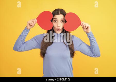 Belle femme étonnante câliner carte papier coeur forme, rêveur isolé sur fond jaune. Concept d'amour. Banque D'Images