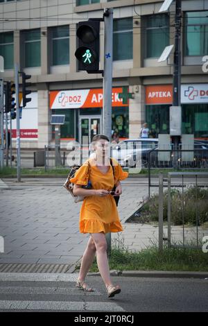 Une femme vêtue d'une robe orange traverse une rue dans le quartier de Praga à Varsovie, Pologne, le 26 août 2022. Banque D'Images