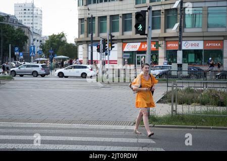 Une femme vêtue d'une robe orange traverse une rue dans le quartier de Praga à Varsovie, Pologne, le 26 août 2022. Banque D'Images