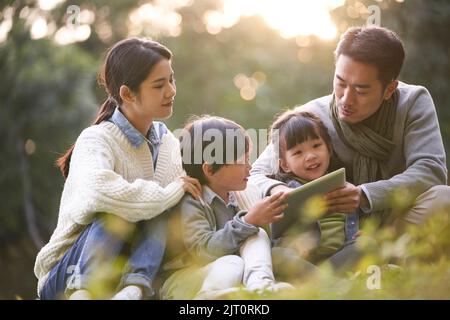 famille asiatique avec deux enfants se détendant à l'extérieur dans le parc de la ville Banque D'Images
